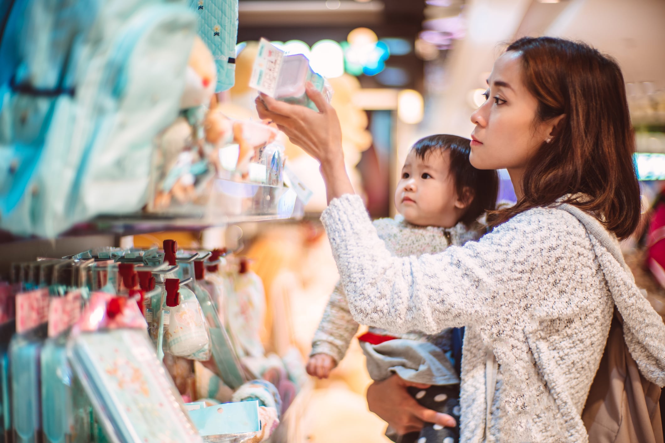 Asian young mother carrying her baby shopping for baby accessories in a shop joyfully.