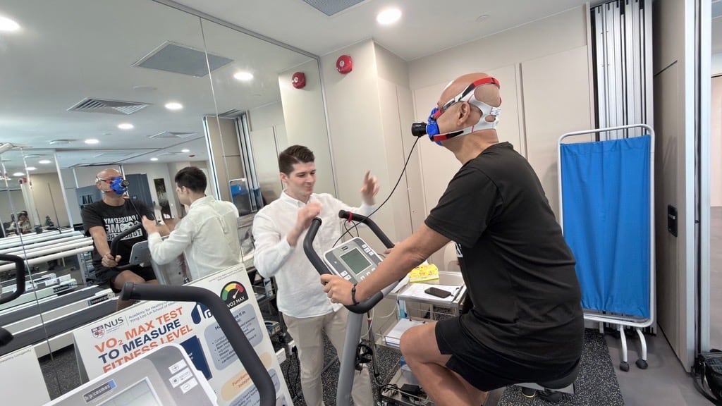 Dr Jozo Grgic (left), from the Academy of Healthy Longevity, guiding Mr Nicholas Singh, the first participant in their PROMETHEUS trial, as they test his stamina and VO2 max on a stationary bicycle in their clinical trial centre’s gym.